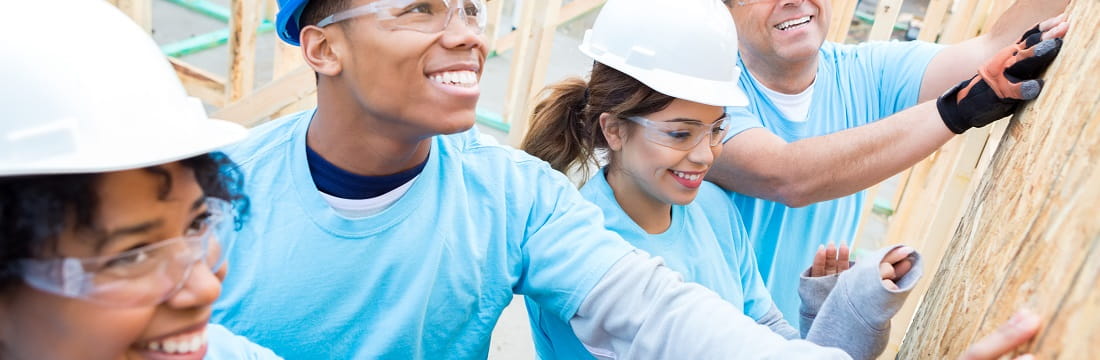 Group of four volunteers in hard hats put the frame of a building together.