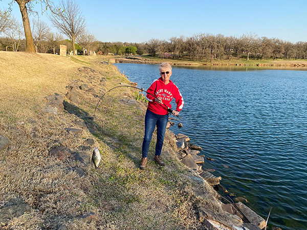 Mary holding a fish she caught in front of the water