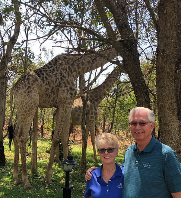 Mary and a man standing in front of a pair of grazing giraffes